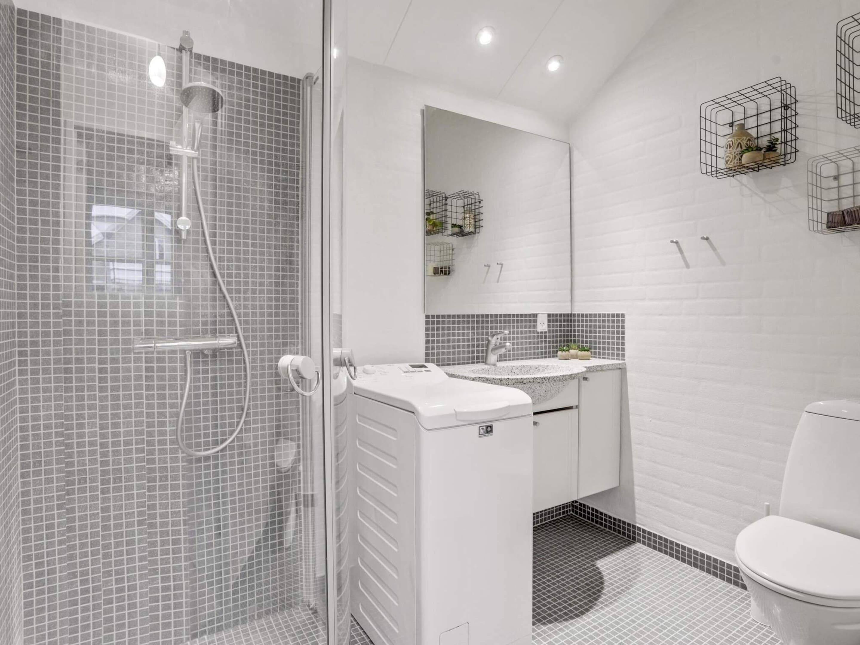 A modern bathroom with a glass-enclosed shower, a white sink with a mirror above it, and a toilet.