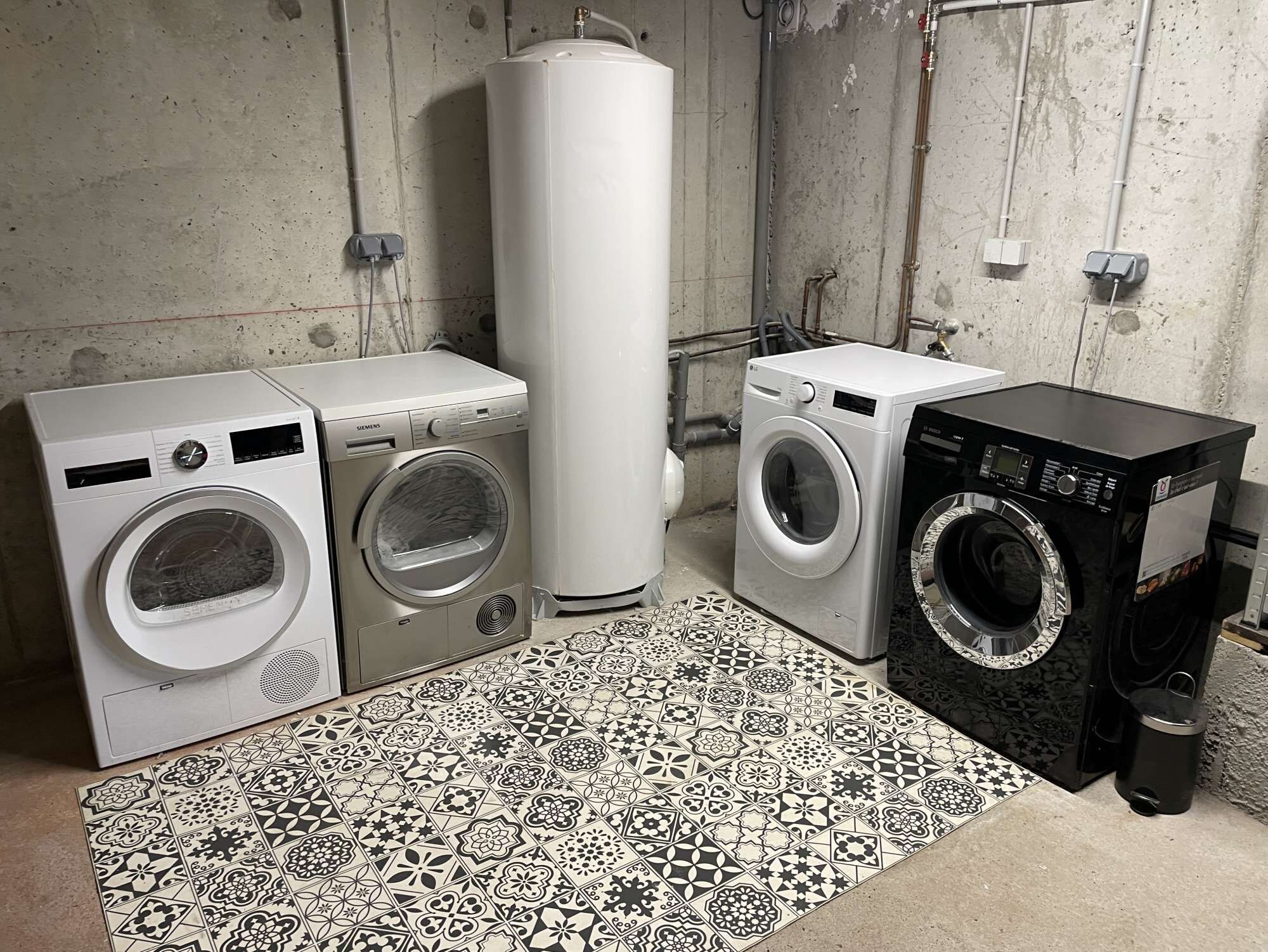 Une buanderie équipée de quatre machines à laver, d’un grand chauffe-eau et d’un sol à motifs.
