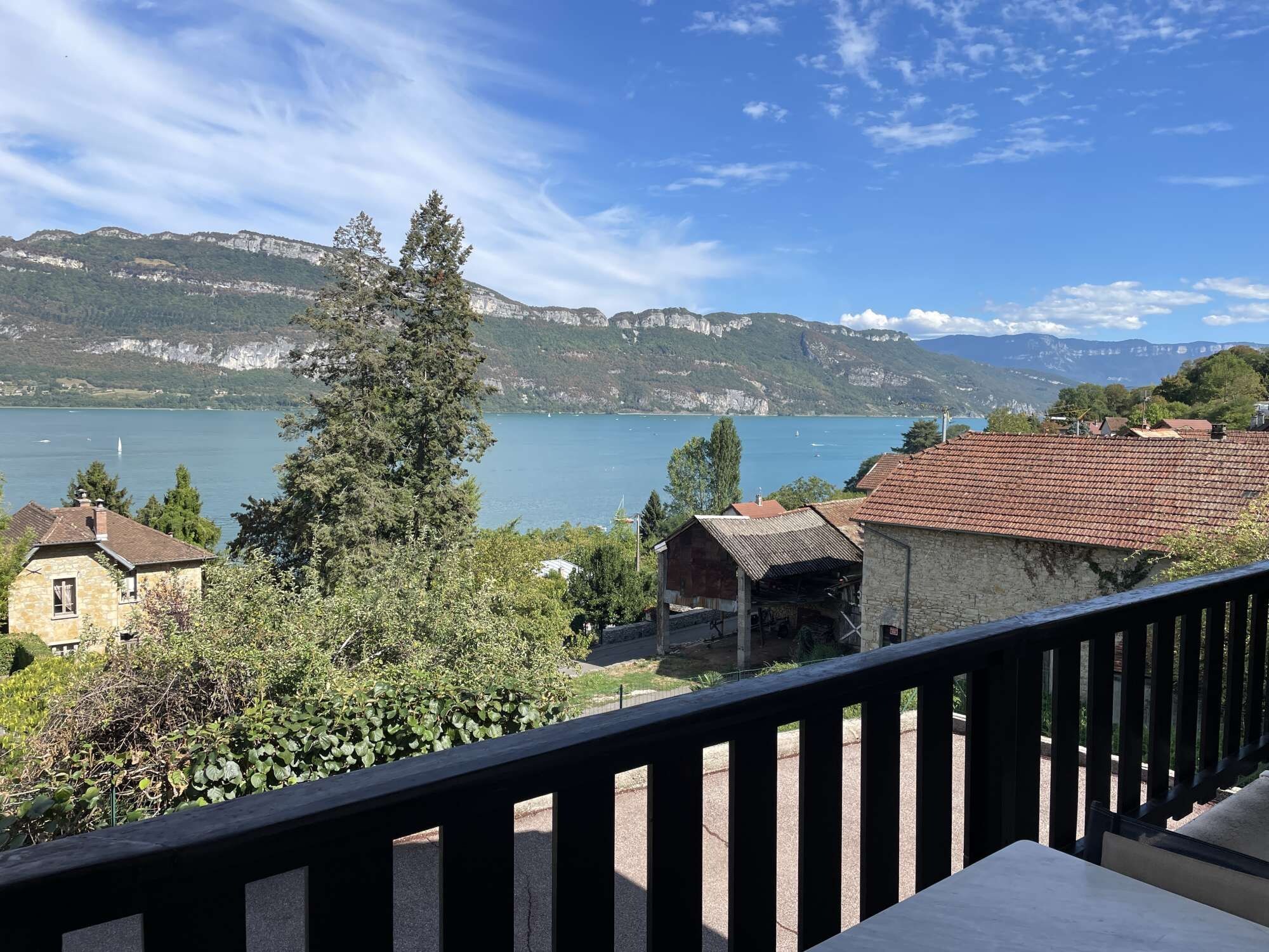 Un balcon avec vue sur un lac, des montagnes et un bâtiment en pierre.
