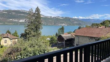 Un balcon avec vue sur un lac, des montagnes et un bâtiment en pierre.