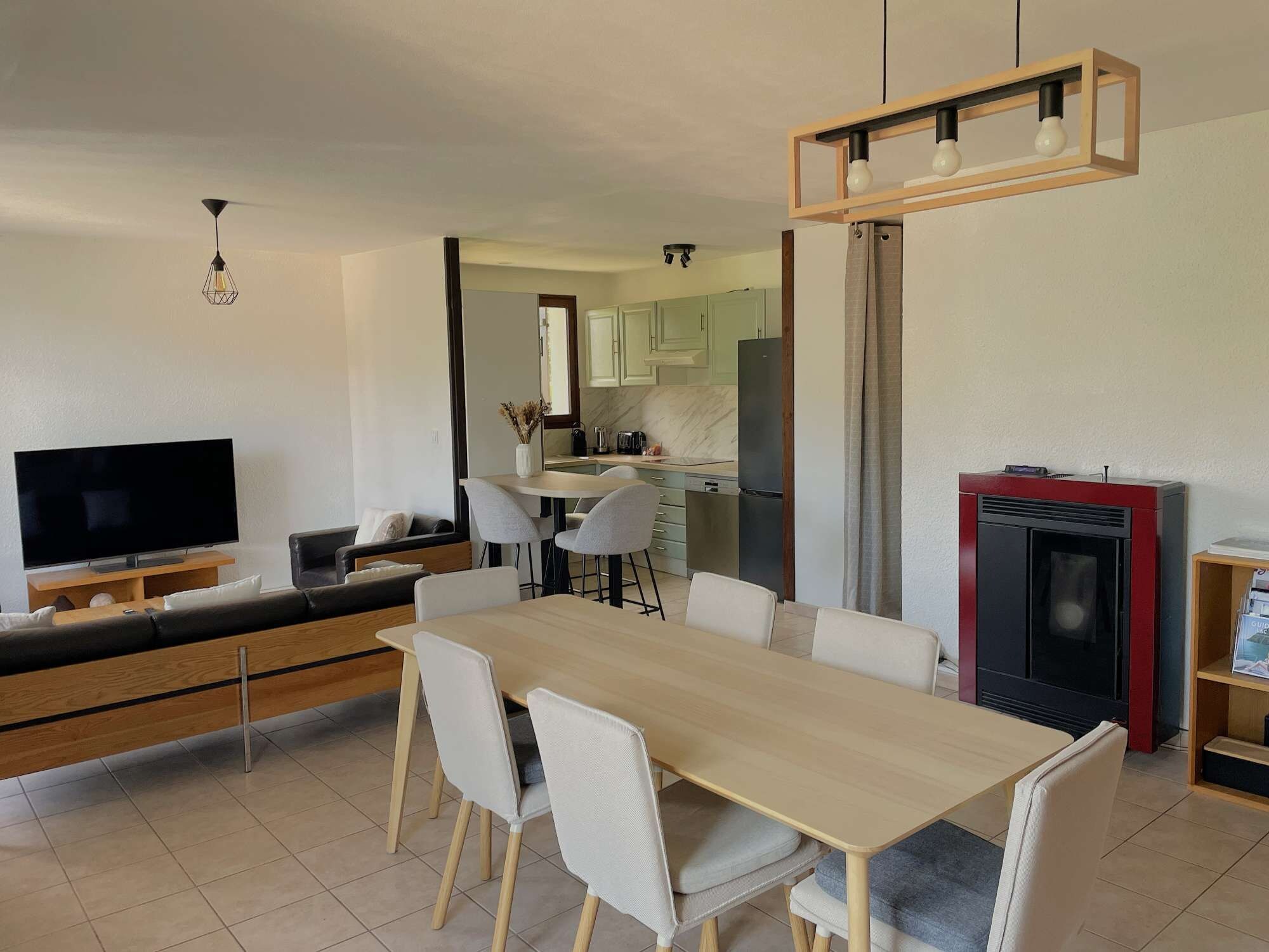 Een moderne woonkamer met een flatscreen televisie, een bank, een eettafel met stoelen, en een keuken met kasten en een koelkast.