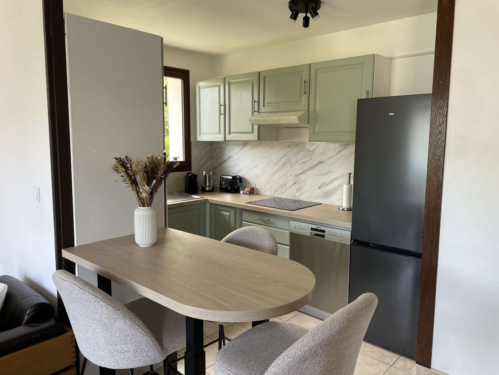 Une cuisine moderne avec une table à manger, des chaises, un réfrigérateur et des meubles de rangement de couleur vert clair.