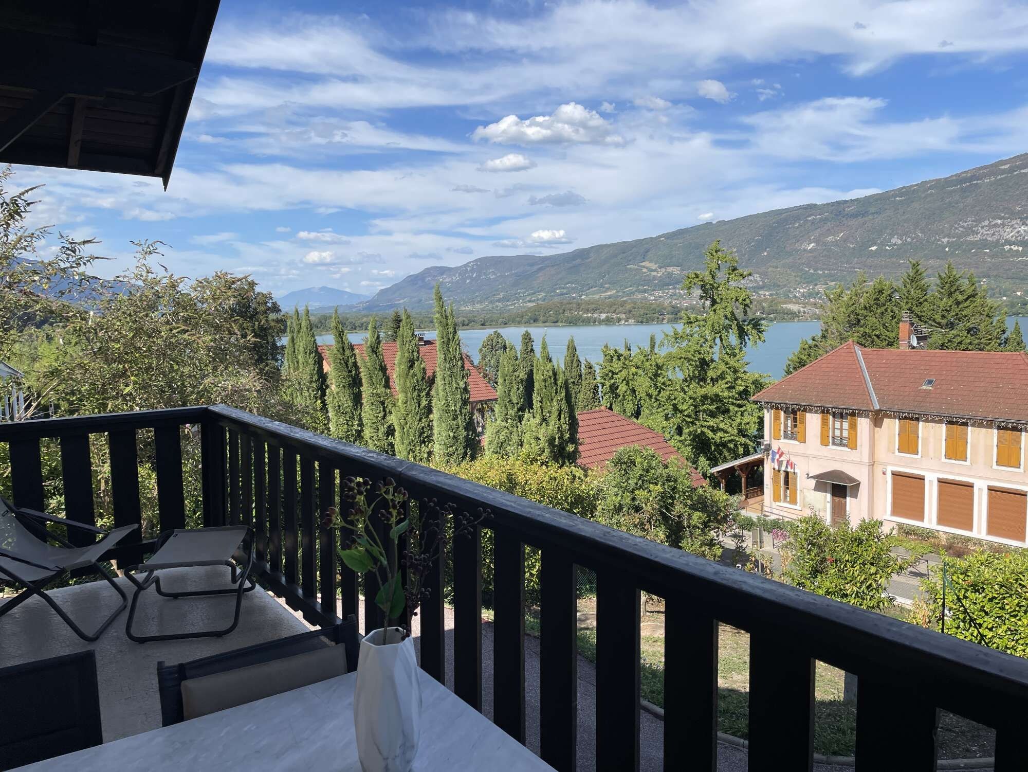 A balcony with a view of a lake, trees, and buildings.