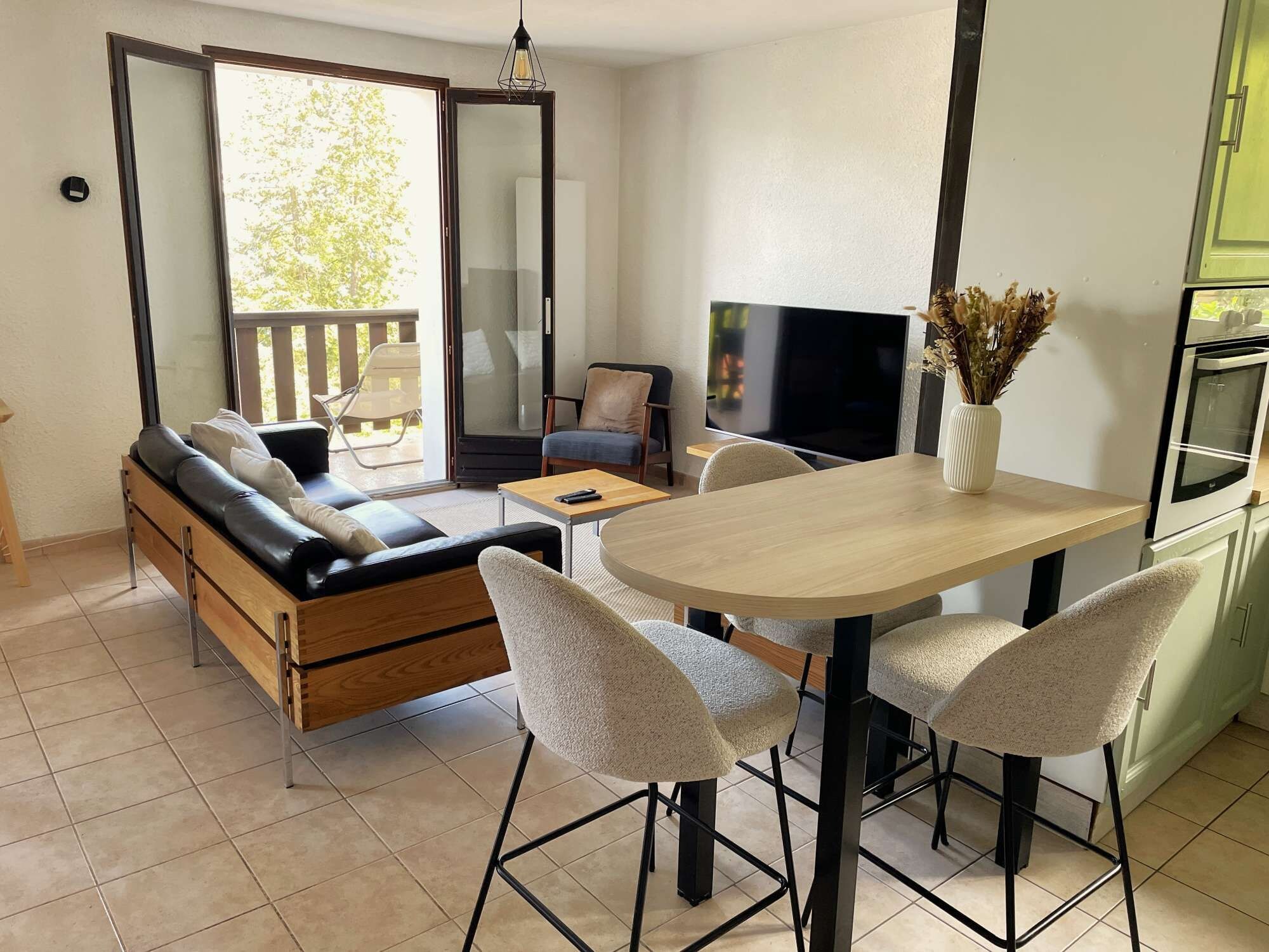 Un espace de vie compact comprenant un canapé, une table à manger avec des chaises, un téléviseur et un coin cuisine.