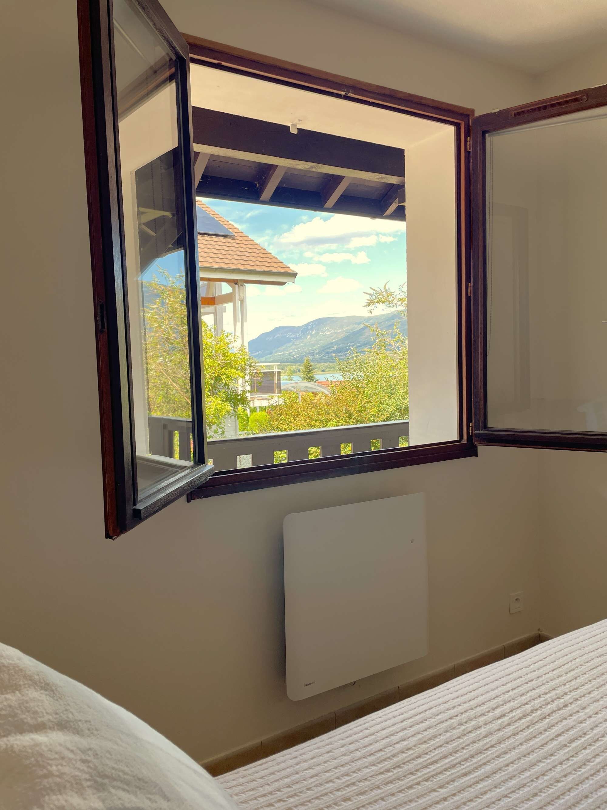Ein Zimmer mit Fenster und Balkonblick, einem weißen Heizkörper und einem Bett.