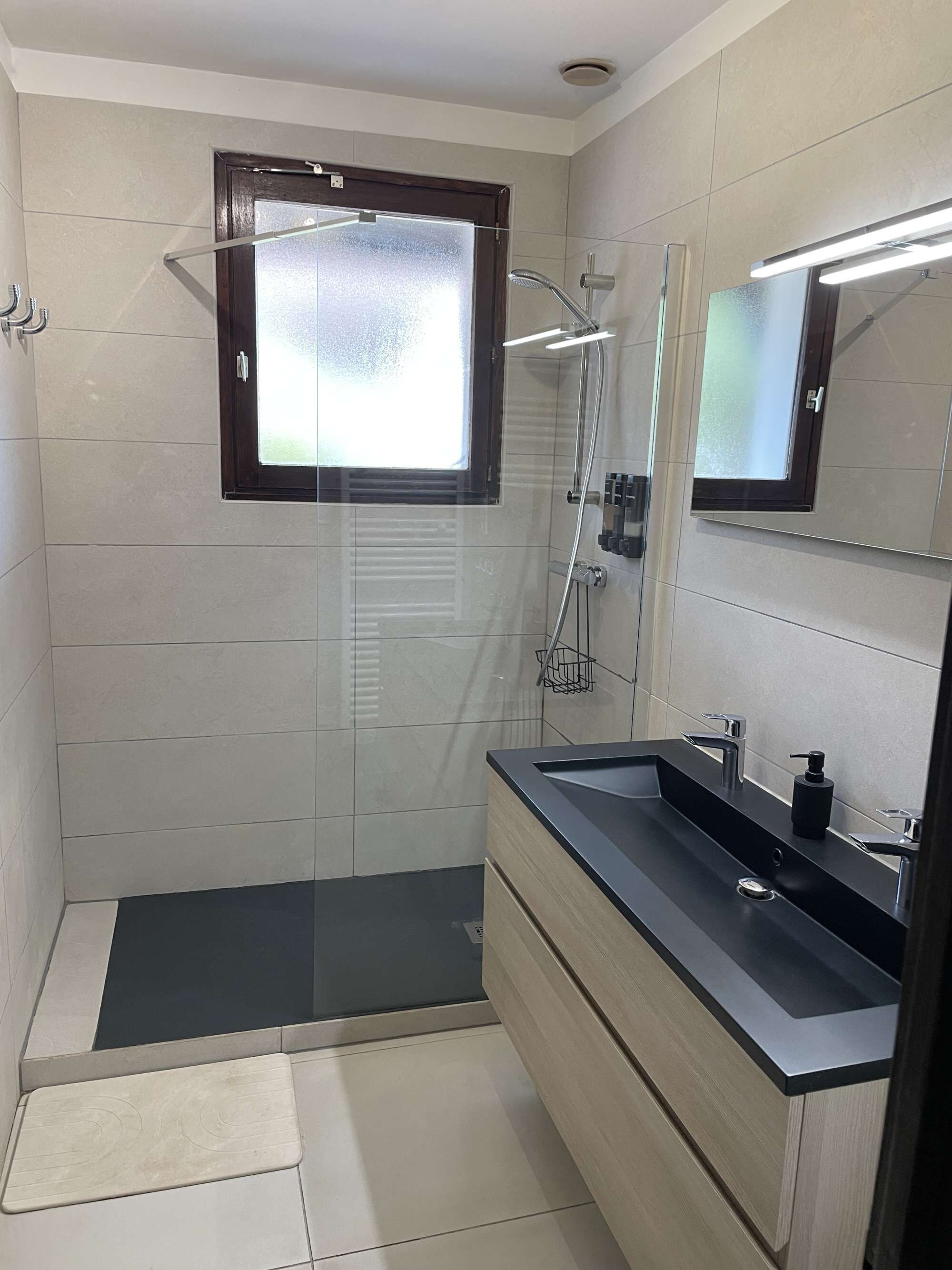 Une salle de bain moderne avec une douche à parois de verre, un meuble-lavabo doté d’un plan de travail noir et un miroir au-dessus du lavabo.