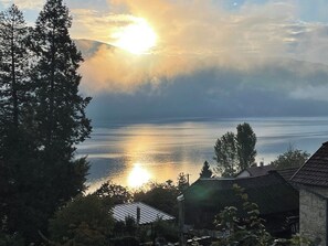 A coastal scene with a house and trees in the foreground, and a body of water reflecting the sun. - Villa with panoramic lake view close to the beach (Conjux)
