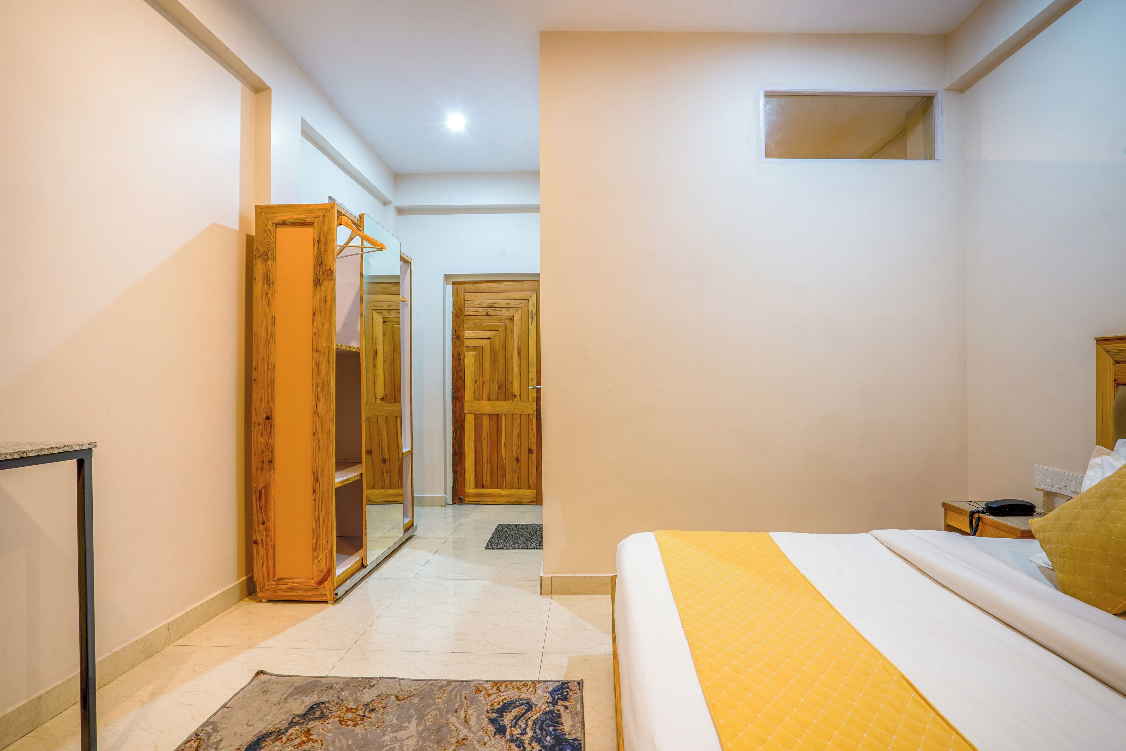 Quarto de hotel com cama, mesa de cabeceira, espelho, guarda-roupa e porta que dá para outro cômodo.