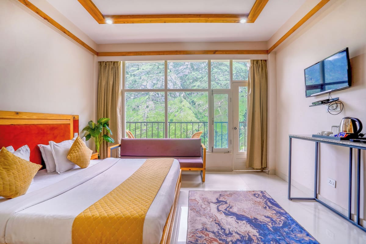 A hotel room with a bed, a sofa, a TV, and a balcony with a view of greenery.