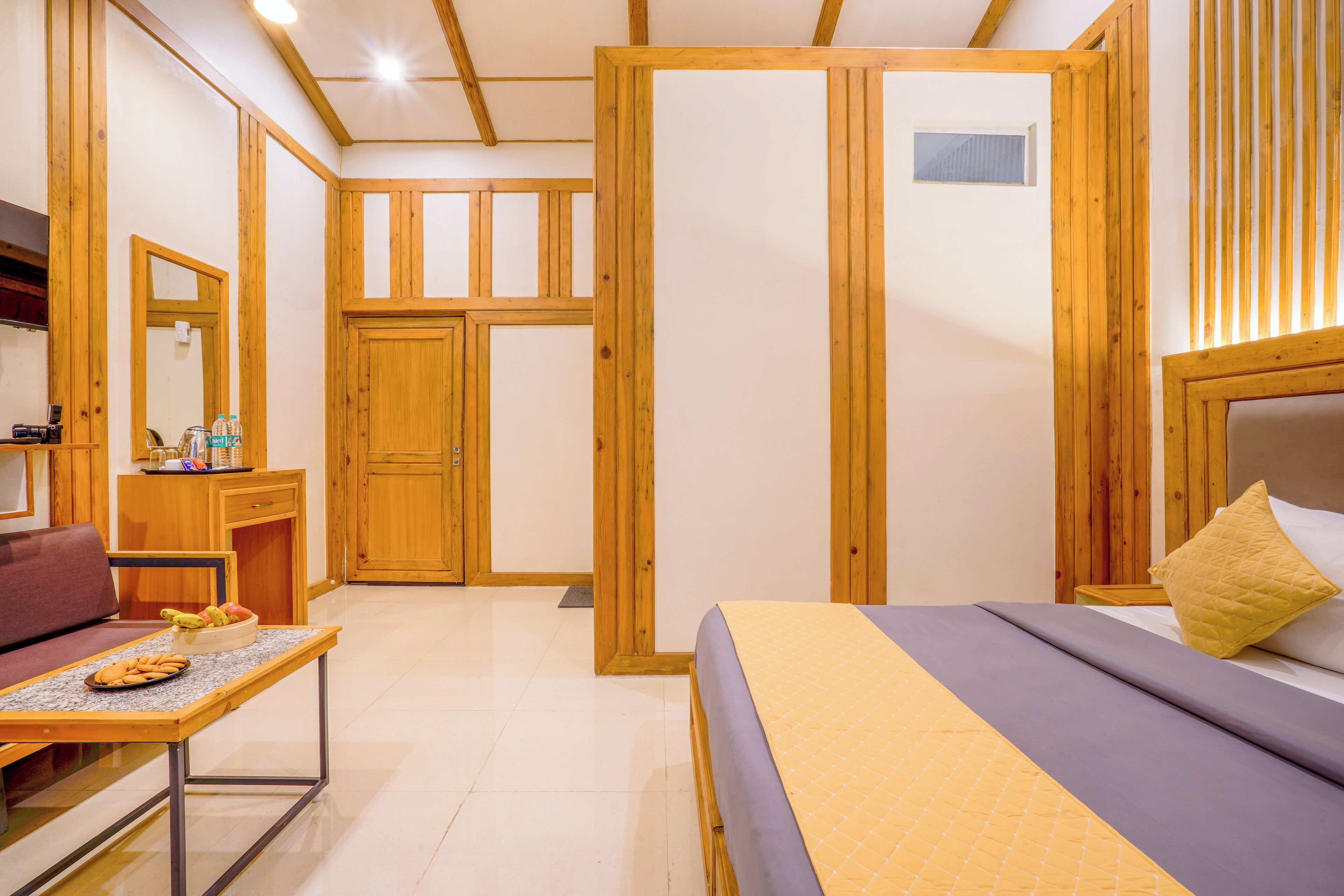 Ein Zimmer mit einem Bett, einem Tisch mit Früchten, einer Couch, einem Schreibtisch und Holzwänden.