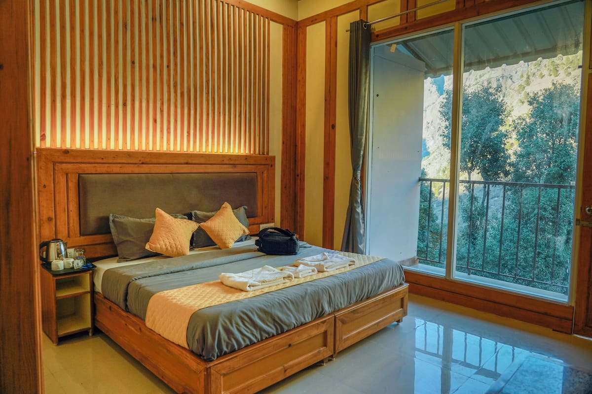 A spacious bedroom with a large bed, wooden headboard, and a view of trees through a balcony.