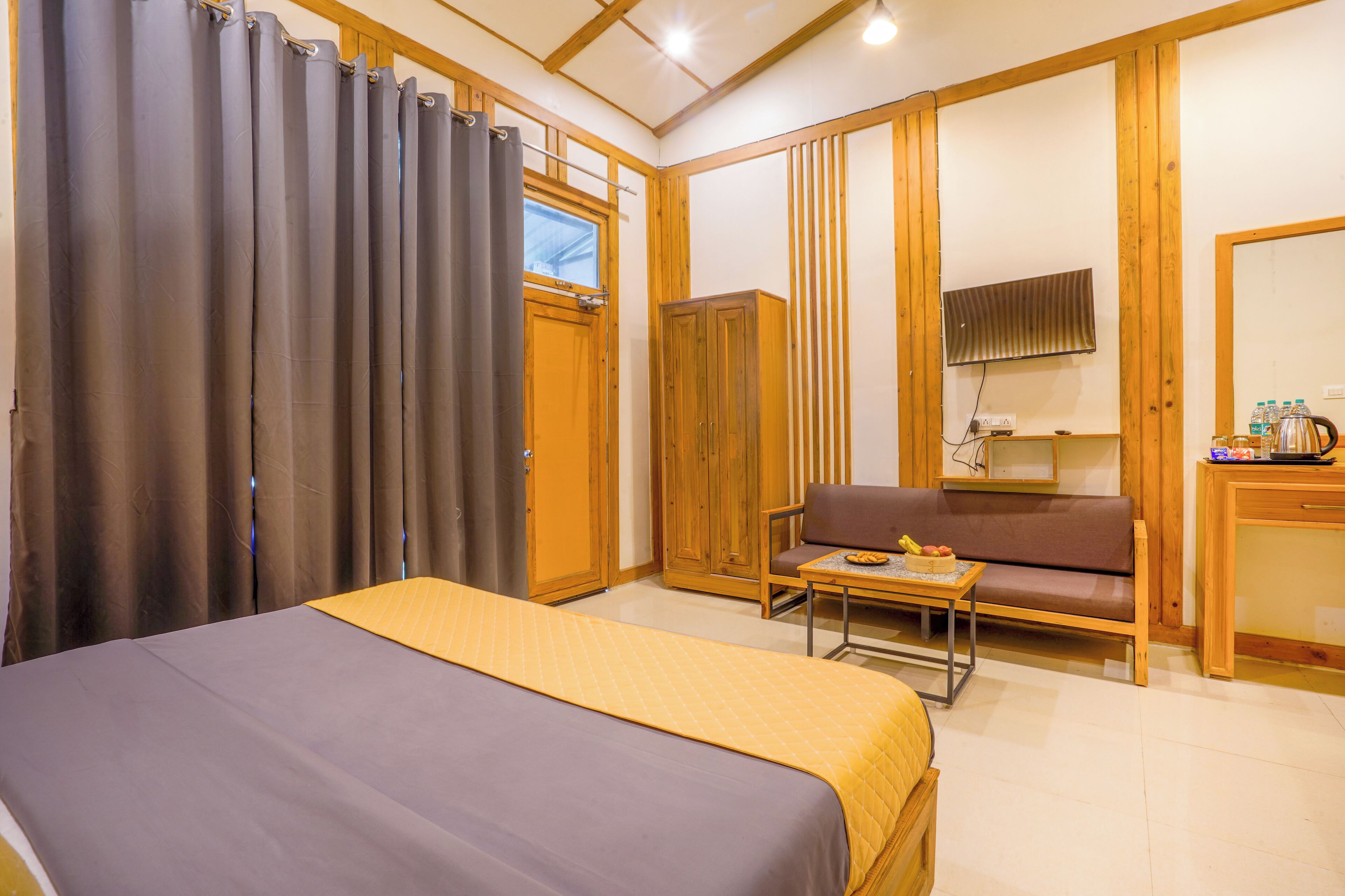 A bedroom with a bed, a wooden wardrobe, a sofa, a small table with a plate of food, and a television on the wall.