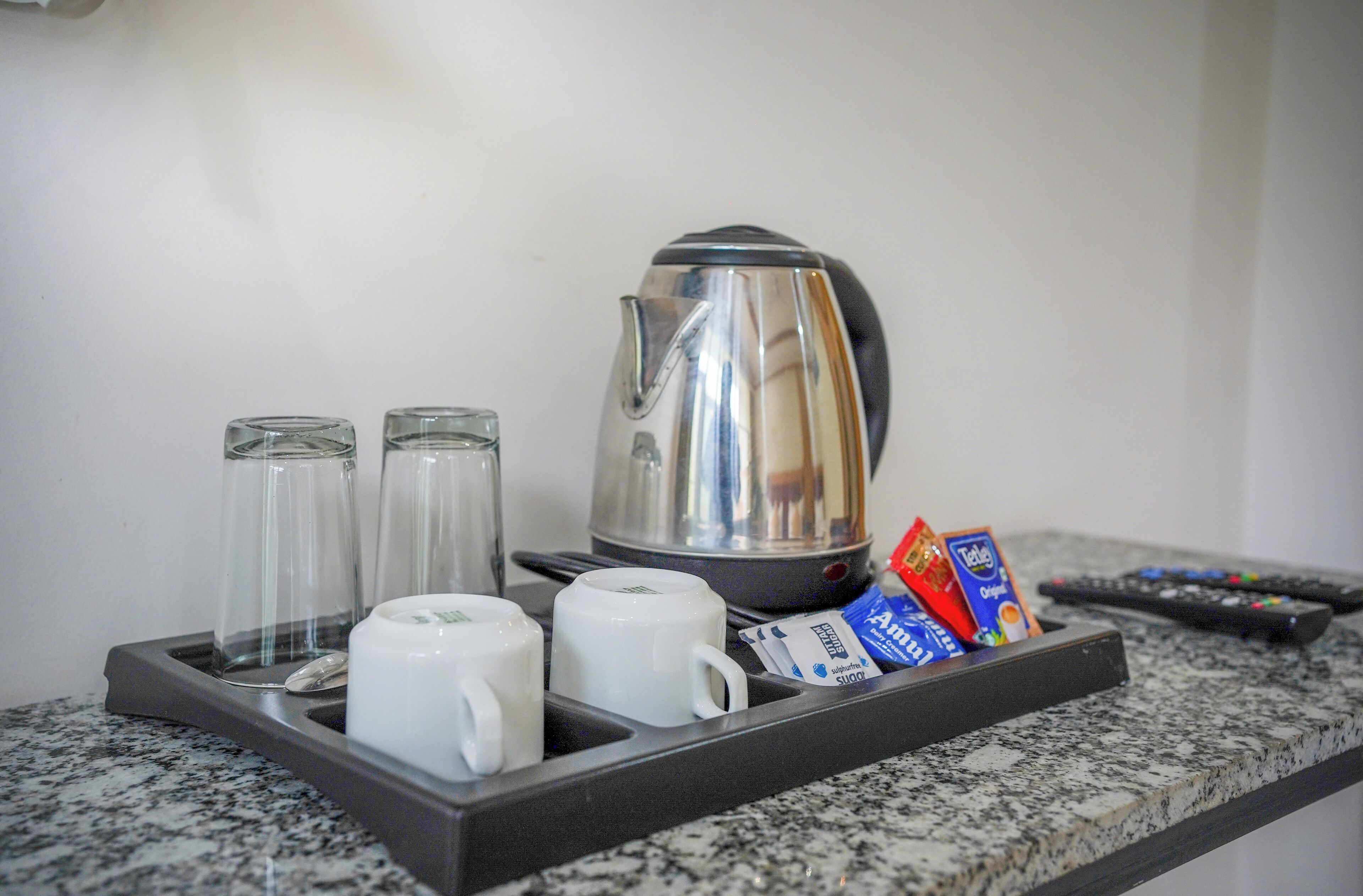 Una encimera de cocina con una cafetera, dos tazas de vidrio, una bandeja con cápsulas de café y un control remoto.