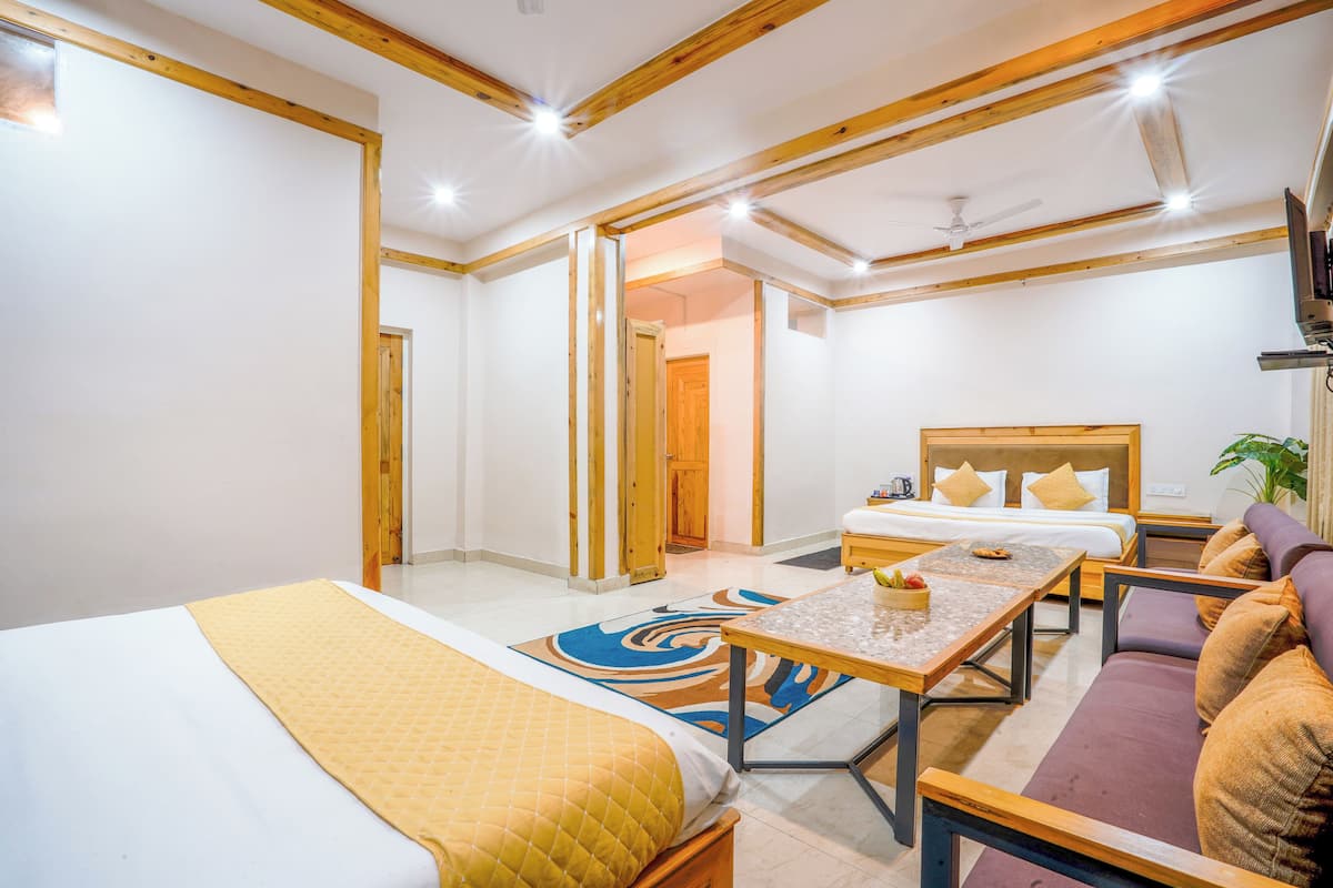 A hotel room with two single beds, a sofa, a dining table, and a TV.