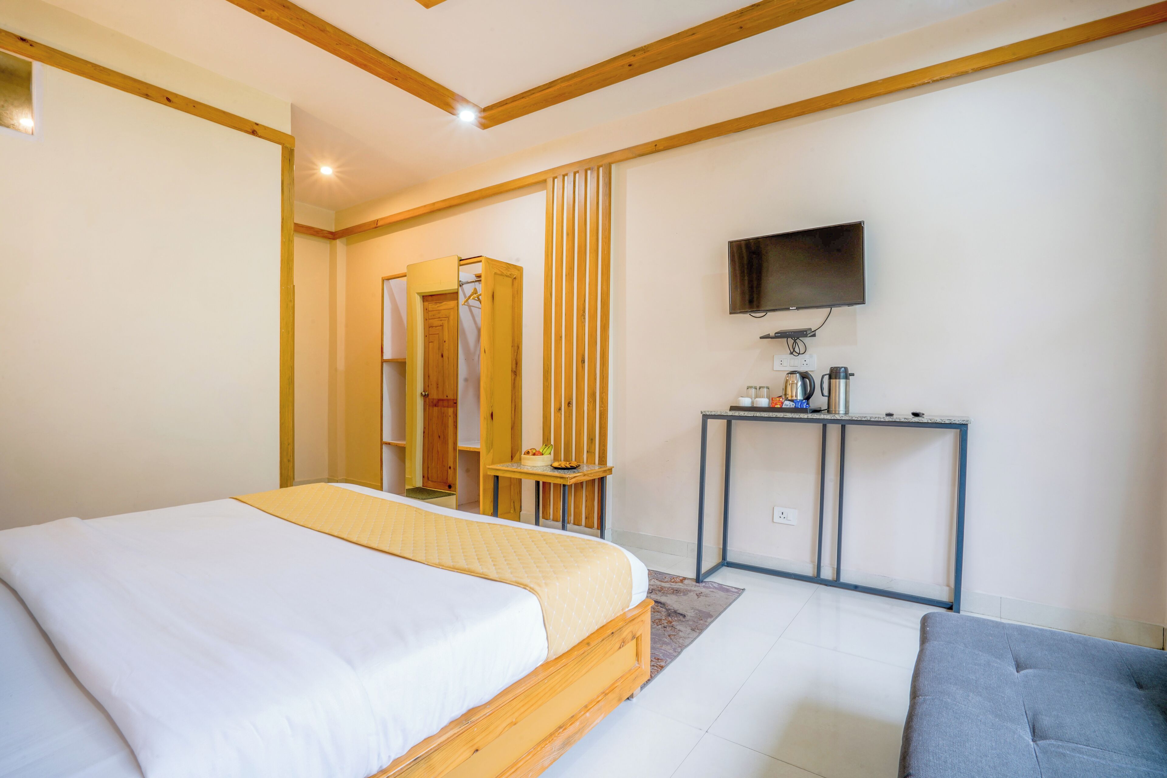 Un dormitorio con una cama de madera, una mesita de noche, un televisor y un pequeño escritorio con una silla.