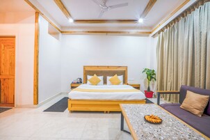 A hotel room with a bed, a sofa, a coffee table, a ceiling fan, and a potted plant.