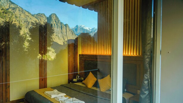 Une chambre avec vue sur la montagne, un lit avec une couette, des oreillers et une table de chevet avec une lampe.