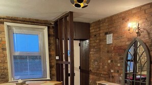 Una habitación con pared de ladrillo, una mesa de comedor de madera con sillas, una estantería y una lámpara de techo original.