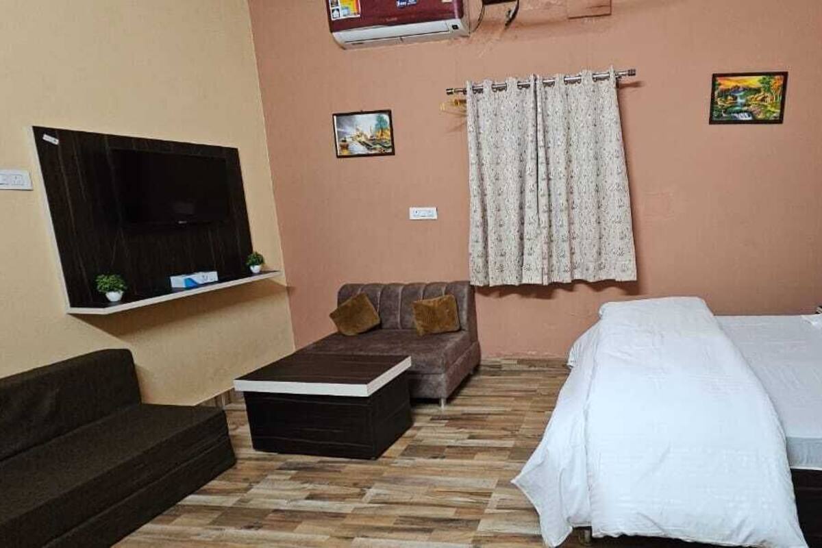 A bedroom with a bed, a sofa, a TV mounted on the wall, and a curtain.
