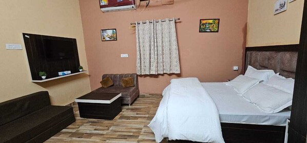 A bedroom with a bed, a sofa, a TV mounted on the wall, and a curtain.