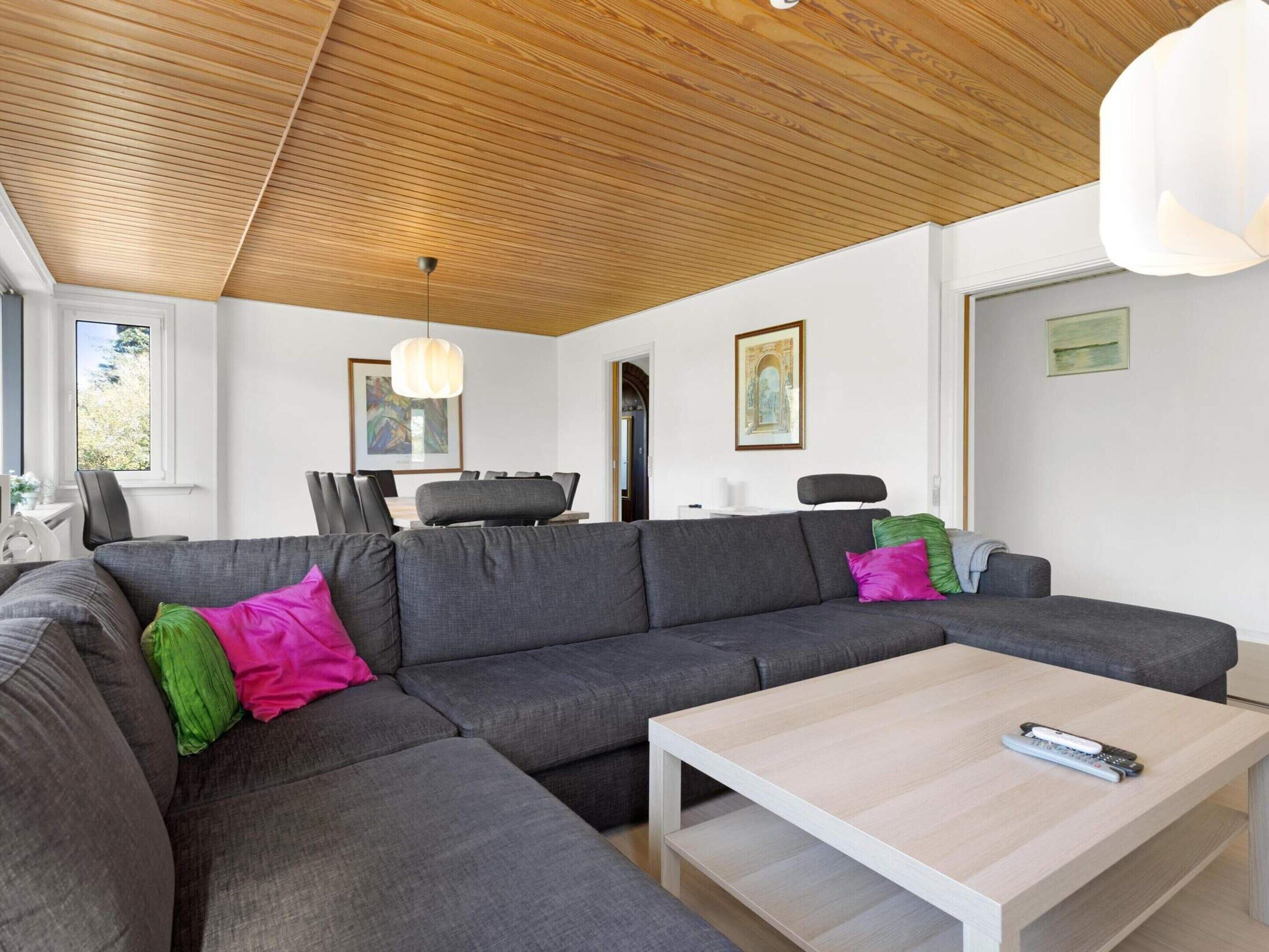 A modern living room with a sectional sofa, a coffee table, and a wooden ceiling.