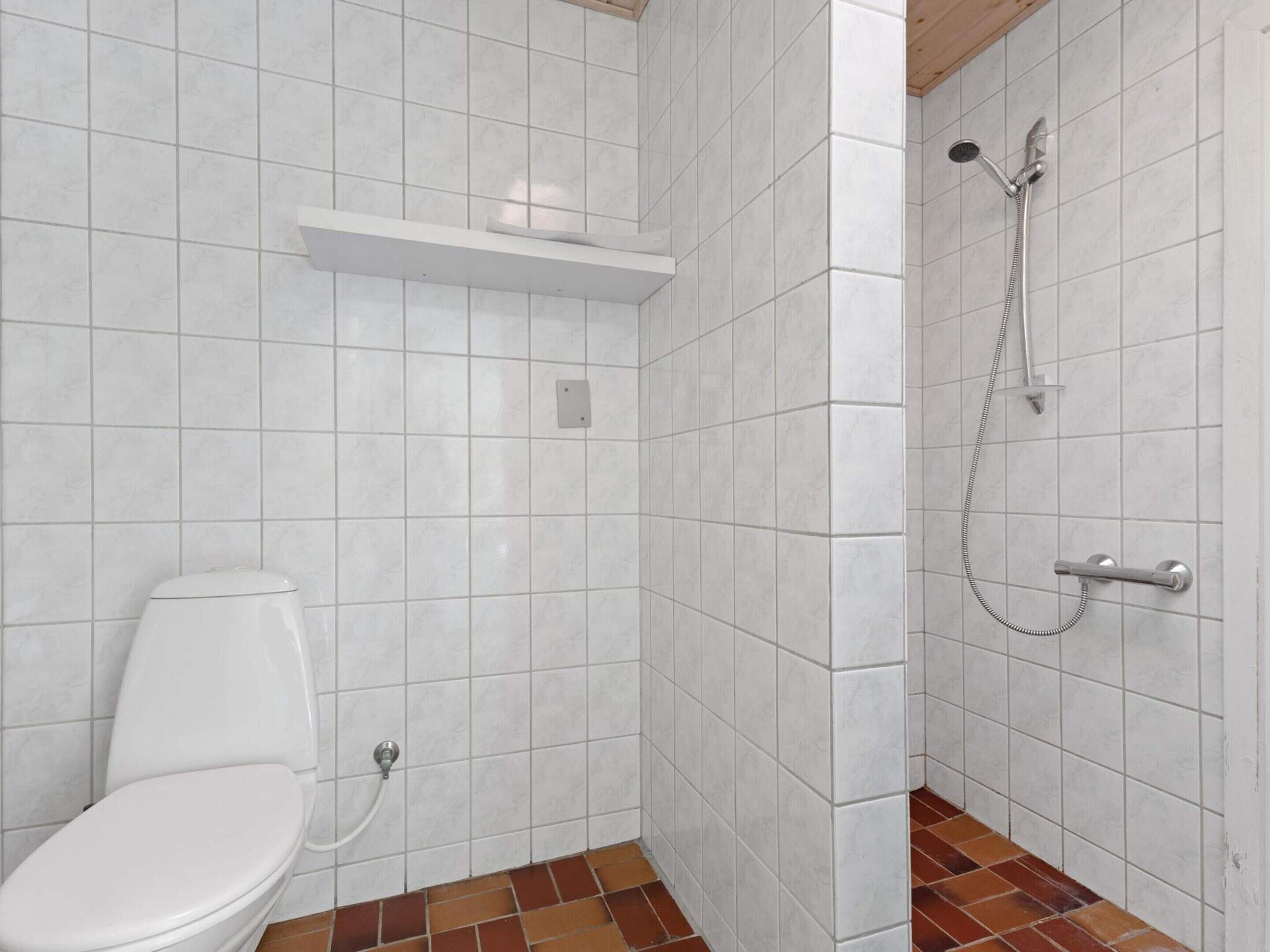 Ein kleines Badezimmer mit Fliesen, einer Toilette, einer Dusche und einem Ablagebrett darüber.