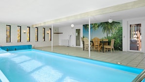 A swimming pool with a tiled deck, a dining area with wicker chairs, and a mural of a tropical scene. - 5 Star Holiday Home in Lokken (Hirtshals)