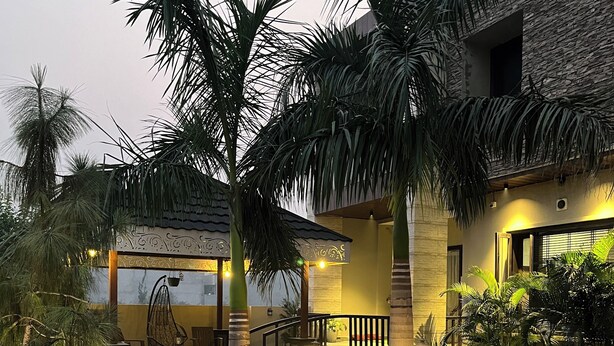 A courtyard with palm trees, outdoor seating, and a stone building.