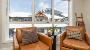 Una habitación con dos sillones de cuero, una pequeña mesa con una planta y vistas a edificios nevados y montañas a través de grandes ventanales.