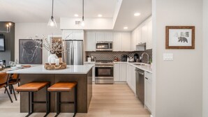 Una cocina moderna con una isla central, electrodomésticos de acero inoxidable e iluminación colgante.