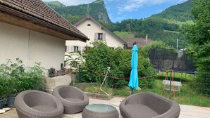 A patio with wicker furniture, a blue umbrella, and a view of a mountain and houses in the background.