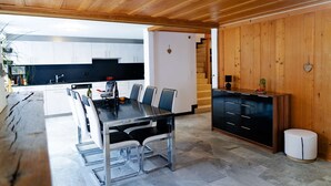 A modern kitchen with a dining area, featuring a large island, white cabinets, and a wooden ceiling.