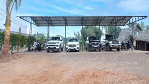 A covered parking area with three vehicles parked under a metal roof. - Anglo Resort (Puducherry)
