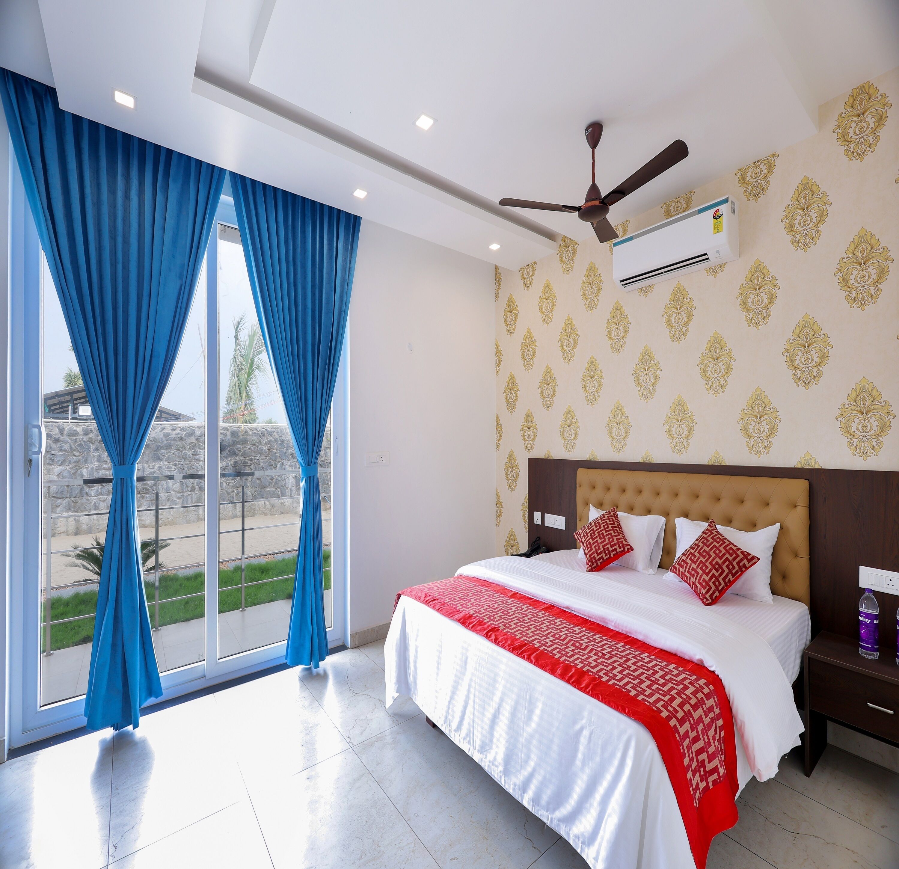 Habitación de hotel con una cama grande, ventilador de techo y vista a la playa desde la ventana.