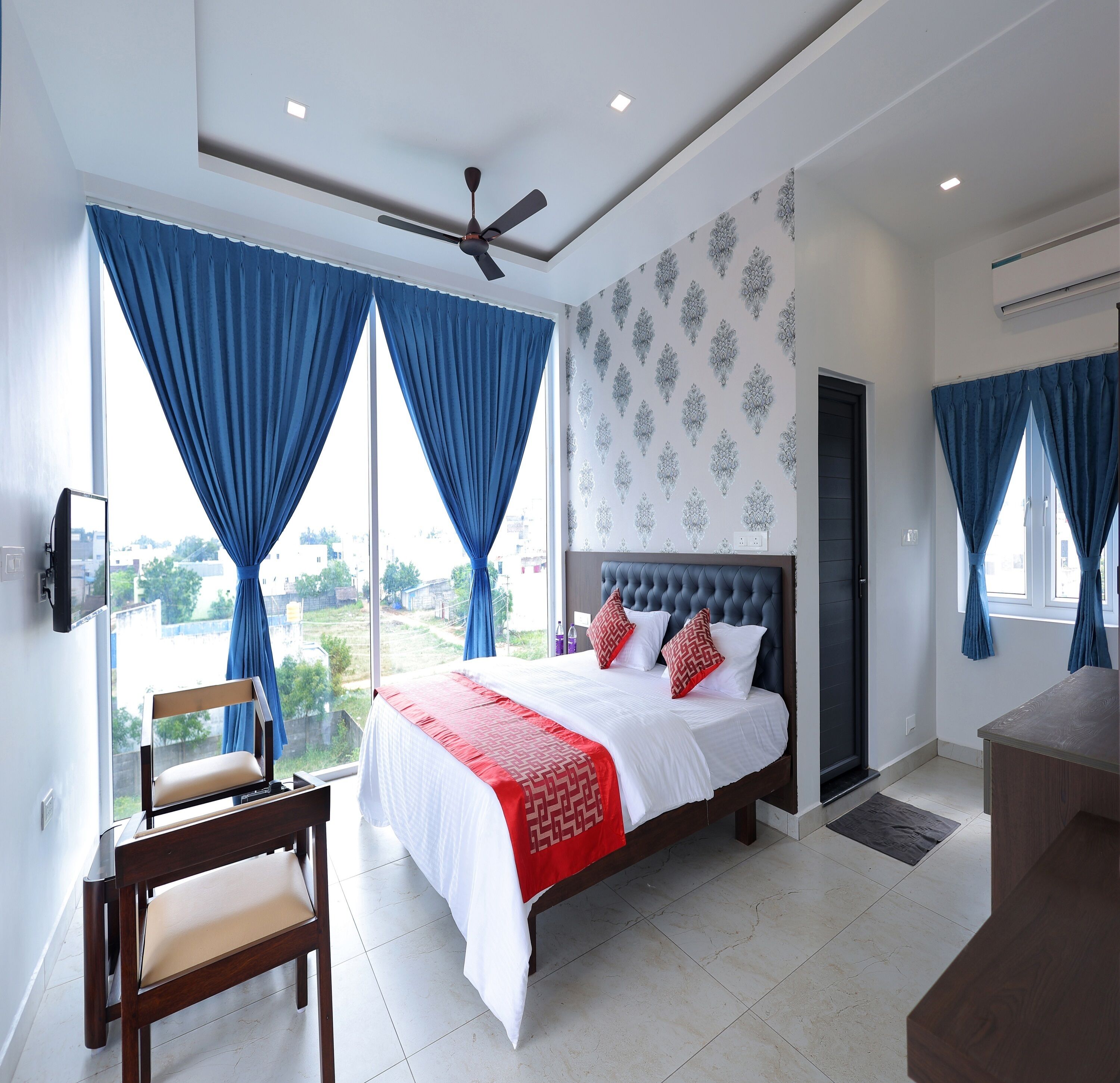 A modern bedroom with a large bed, a ceiling fan, and a view of the city.
