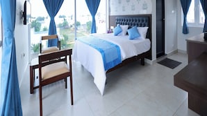 A bedroom with a large bed, a chair, a ceiling fan, and a view of the outside. - Anglo Resort (Puducherry)