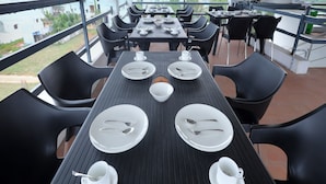 A covered outdoor dining area with tables set for four, each with plates, cutlery, and cups. - Anglo Resort (Puducherry)