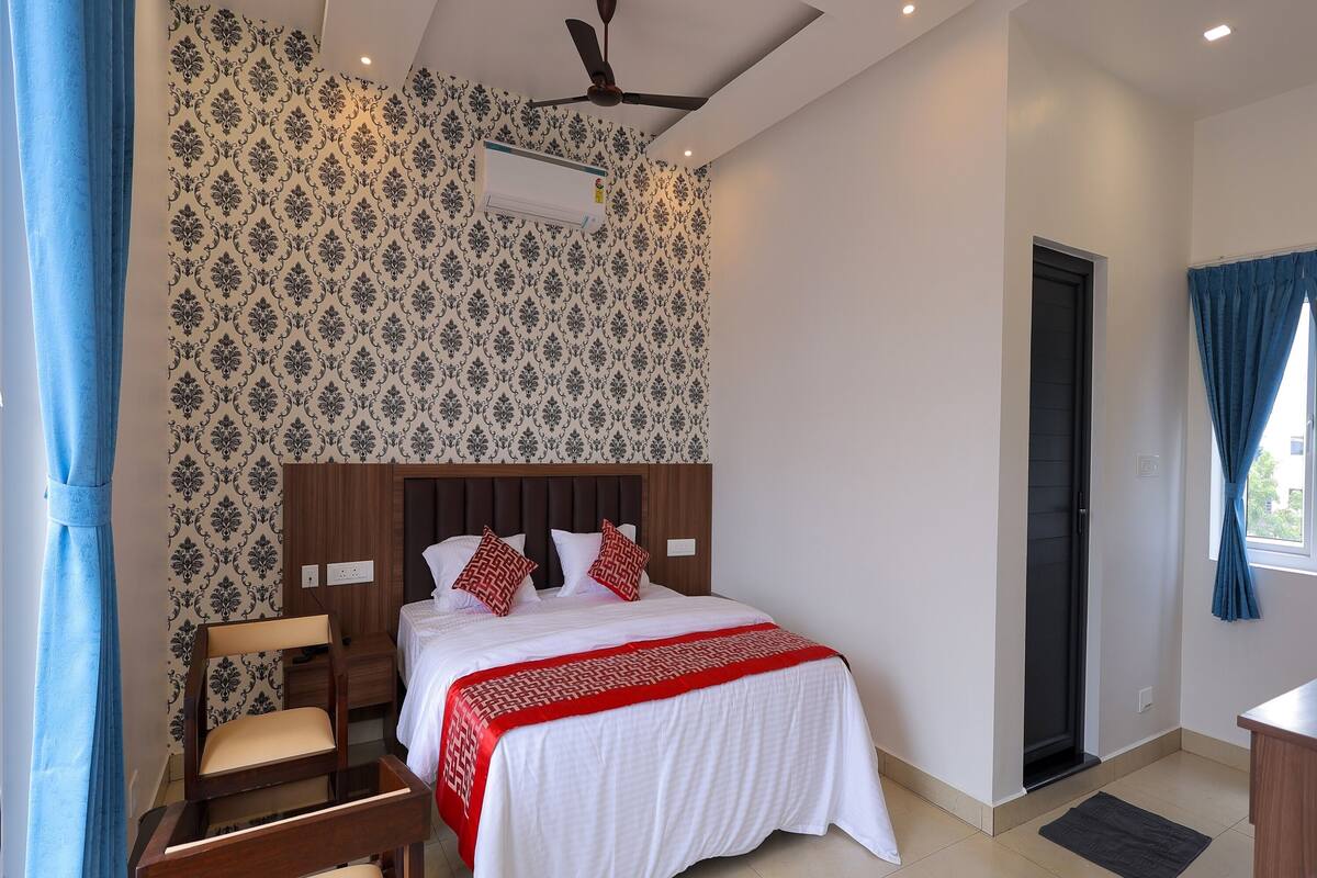 A hotel room with a bed, a desk, a chair, a ceiling fan, and a door.