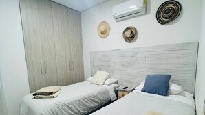 A bedroom with two beds, a wardrobe, an air conditioner, and decorative hats on the wall. - Stunning 2BR Apartament With Pool in Santa Marta (Santa Marta)