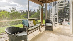 A covered outdoor seating area with wicker furniture, a staircase, and a pool in the background.