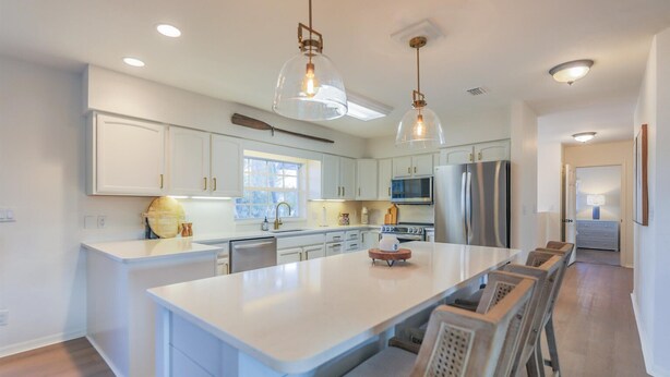 A modern kitchen with white cabinetry, a large island, stainless steel appliances, and pendant lighting.