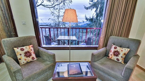 Ein Zimmer mit zwei Sesseln, einem kleinen Tisch und Blick auf einen Balkon mit Tisch und Stühlen.