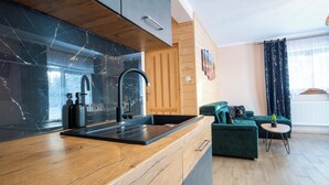 Una cocina moderna con encimera de mármol negro, armarios de madera y un sofá verde en la zona de estar.