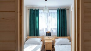 Una habitación con dos camas de madera, una mesita de noche con lámpara y una ventana con cortinas.