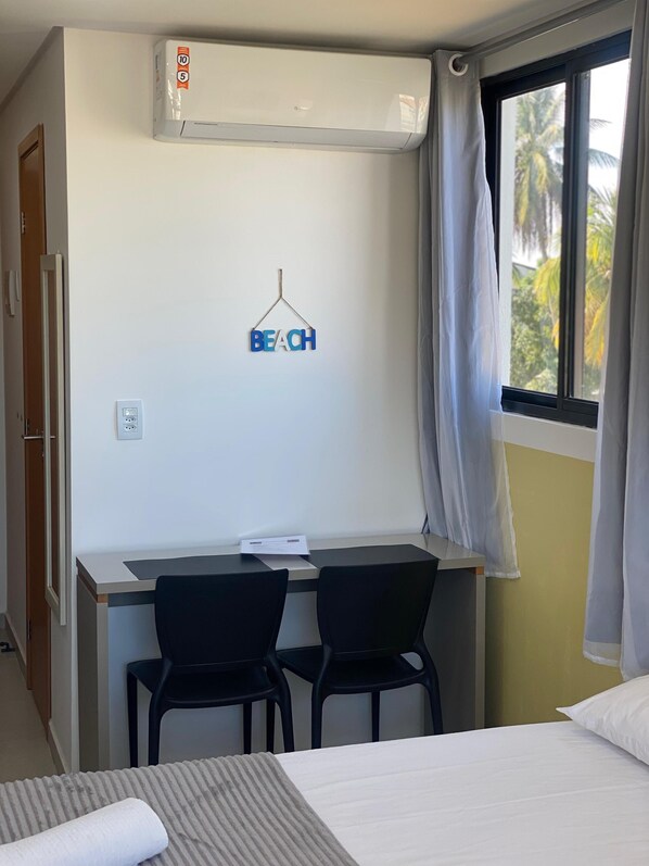 Una camera d'albergo con una scrivania, due sedie, un letto e una finestra con tende.