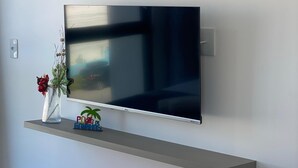 A flat-screen TV mounted on a wall above a grey shelf. - Flat 114 Centro Porto de Galinhas bLP (Ipojuca)