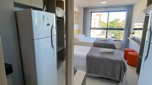 A modern hotel room with a kitchenette, two beds, a large window, and a view of the outside. - Flat 114 Centro Porto de Galinhas bLP (Ipojuca)