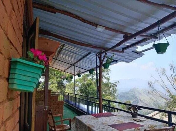 Un espacio al aire libre cubierto con una mesa, sillas, plantas en macetas y vistas a las montañas.