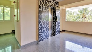 A spacious hallway with a polished floor, a decorative wall with a stone pattern, and a large window with a view of palm trees. - Family Castle Hotel & Restaurant (Thiruvananthapuram)