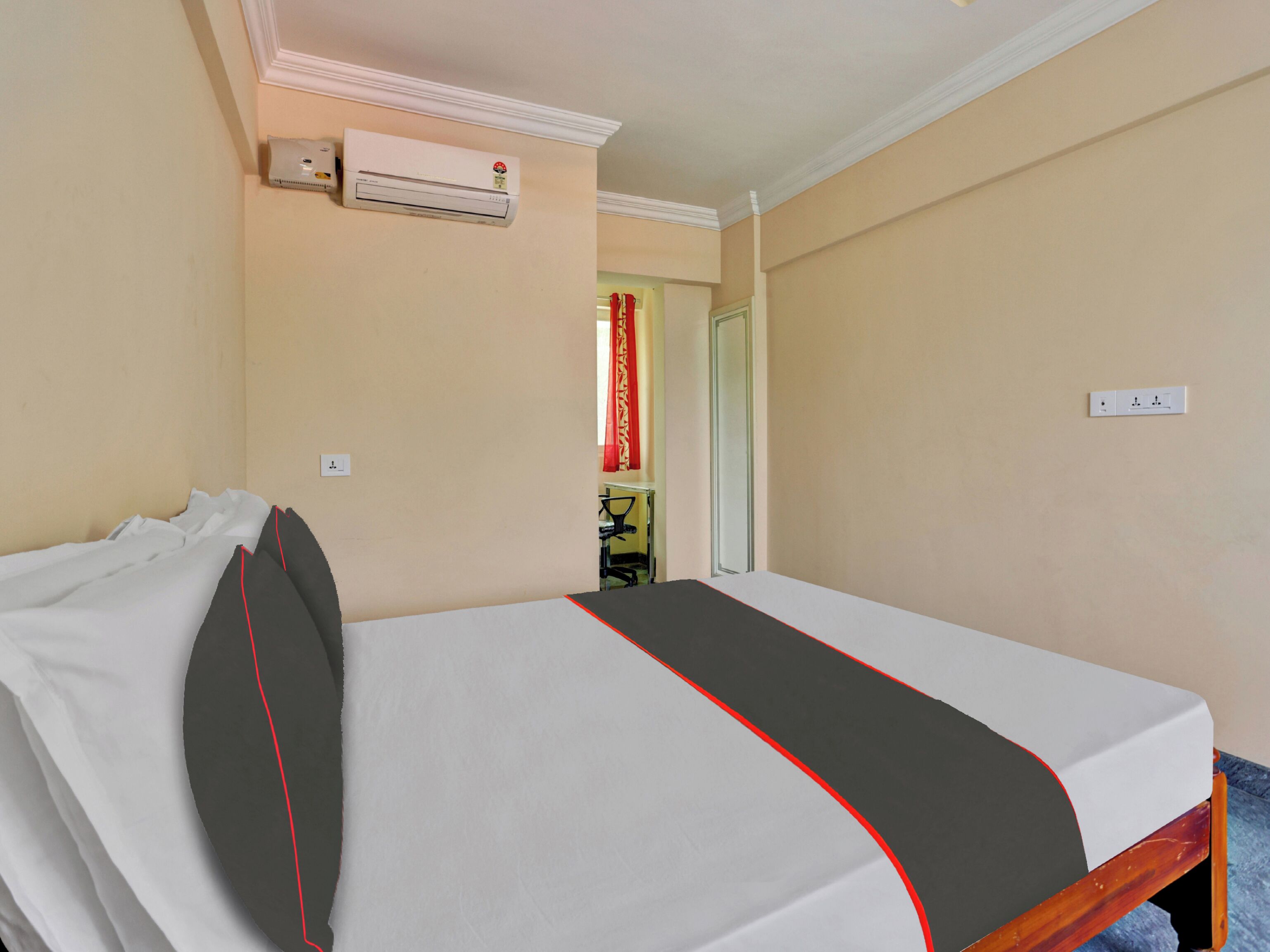 Une chambre d’hôtel avec un lit simple, un appareil de climatisation, un miroir et une porte avec un rideau rouge.